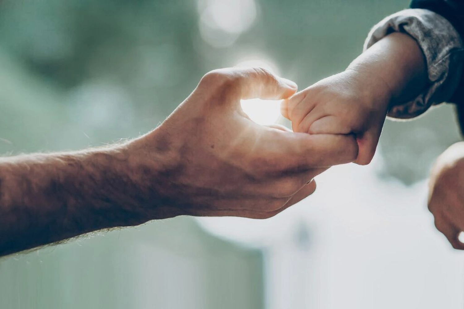 Atrium Sports e.V. - Kampfsport und Fitness – eine Nahaufnahme der Hand eines Erwachsenen und der Hand eines Kindes, die durch ihre kleinen Finger verbunden sind, eine Geste, die allgemein als kleines Versprechen oder kleiner Fluch gilt