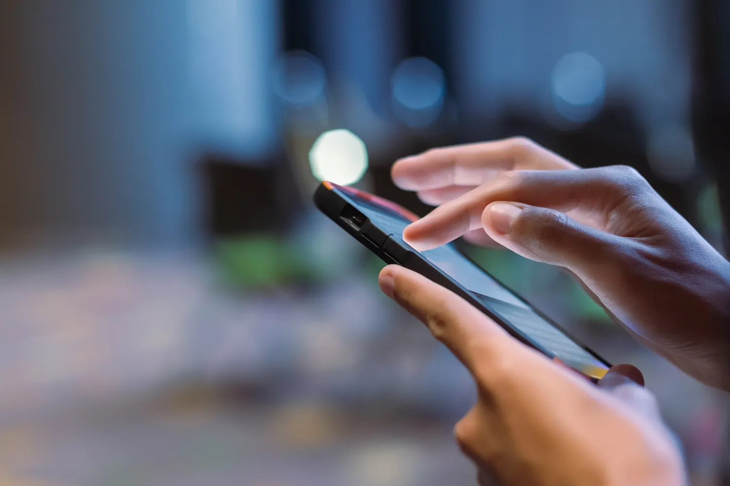 Atrium Sports e.V. - Kampfsport und Fitness - Nahaufnahme einer männlichen Hand mit Smartphone im Besprechungsraum, verschwommener Bokeh-Hintergrund. Durchsuchen von Datennetzen oder Online-Chatten.